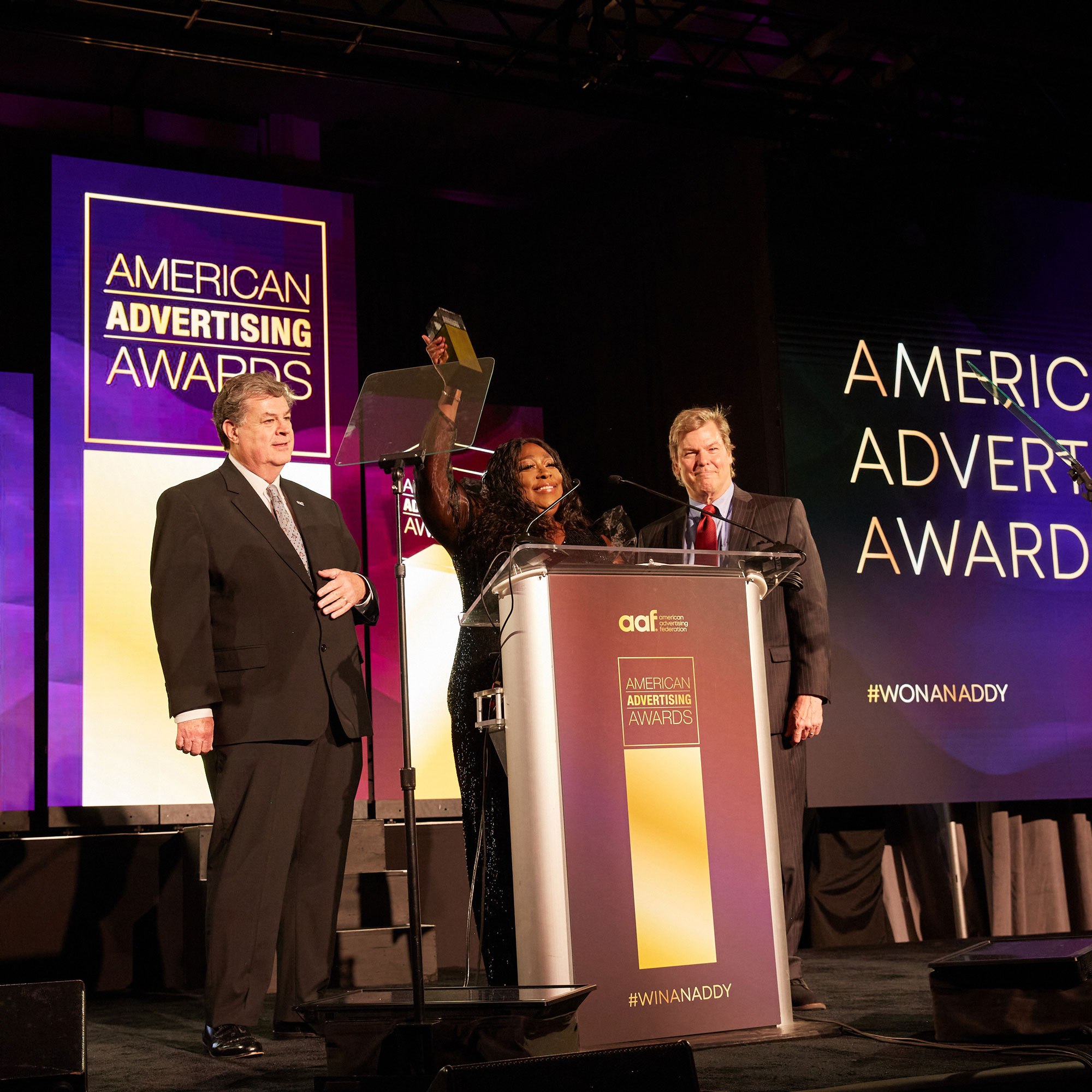 Host and comedian Loni Love holding an ADDY with Steve Pacheco and David Campbell at the 2023 American Advertising Awards Gala